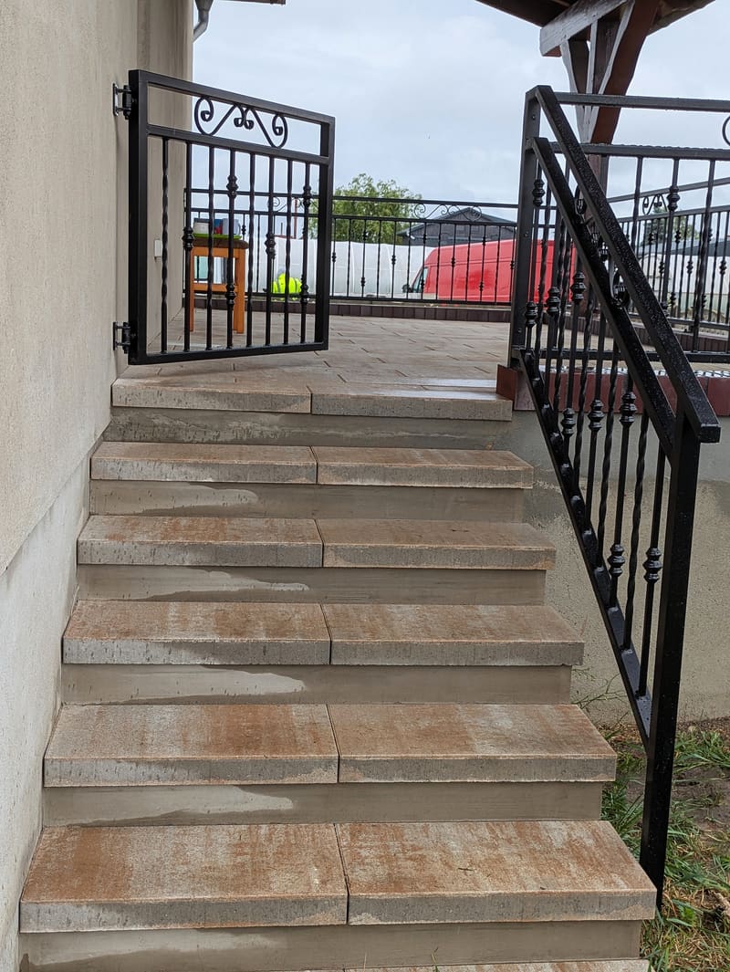 Kuta balustrada schodów prowadzących na taras, u góry furtka z ozdobnym zwieńczeniem