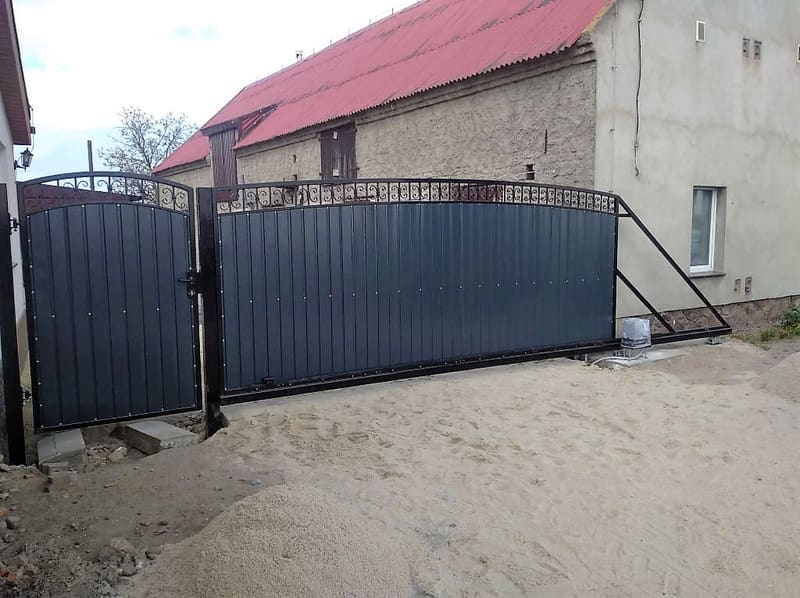 Brama przesuwna z pełnym wypełnieniem w kolorze antracytowym przy budynku gospodarczym