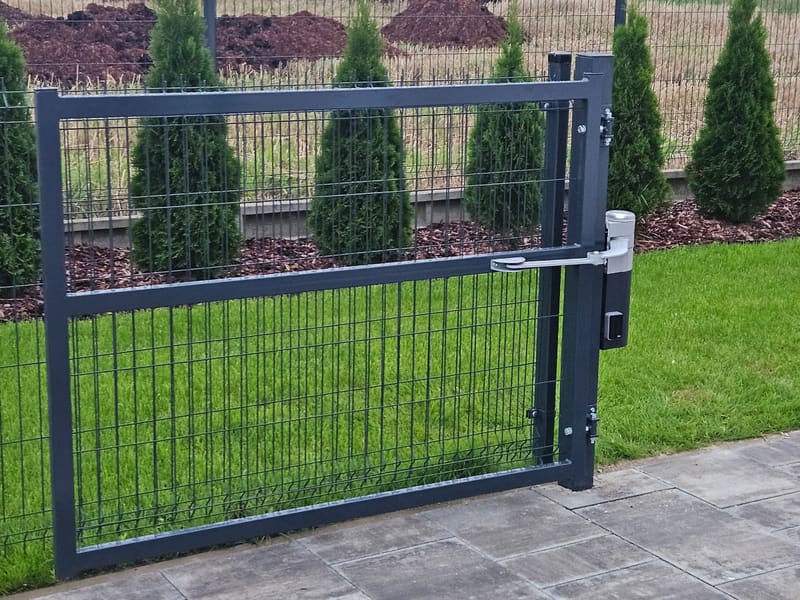 Furtka z panelu ogrodzeniowego z napędem ramieniowym na słupku, widok od strony ogrodu