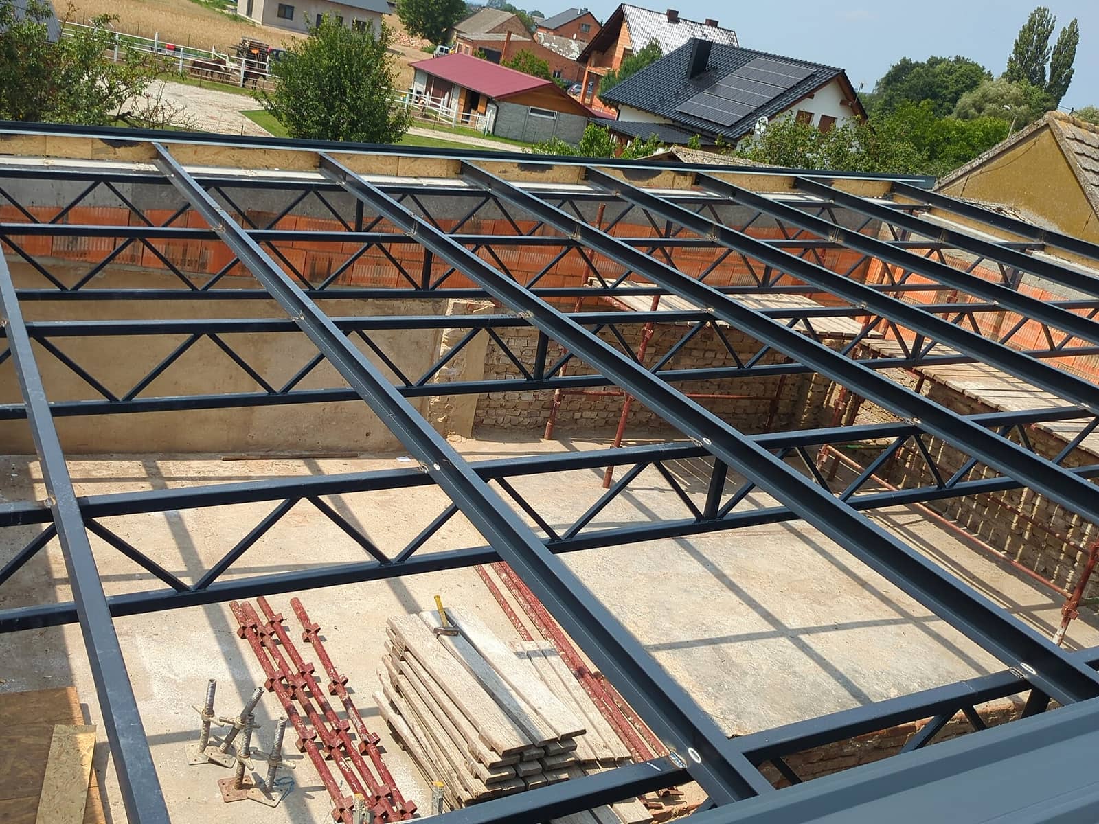 Stalowe kratownice i płatwie konstrukcji dachu nad budowanym budynkiem, widok z góry
