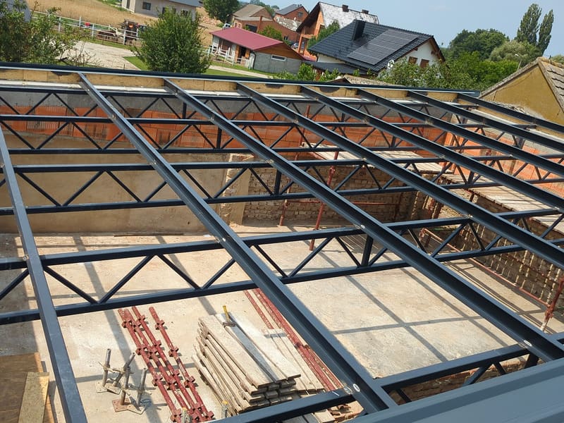 Stalowe kratownice i płatwie konstrukcji dachu nad budowanym budynkiem, widok z góry