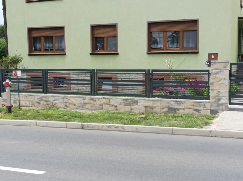 Ogrodzenie frontowe z poziomych lameli biegnące wzdłuż drogi przy domu jednorodzinnym