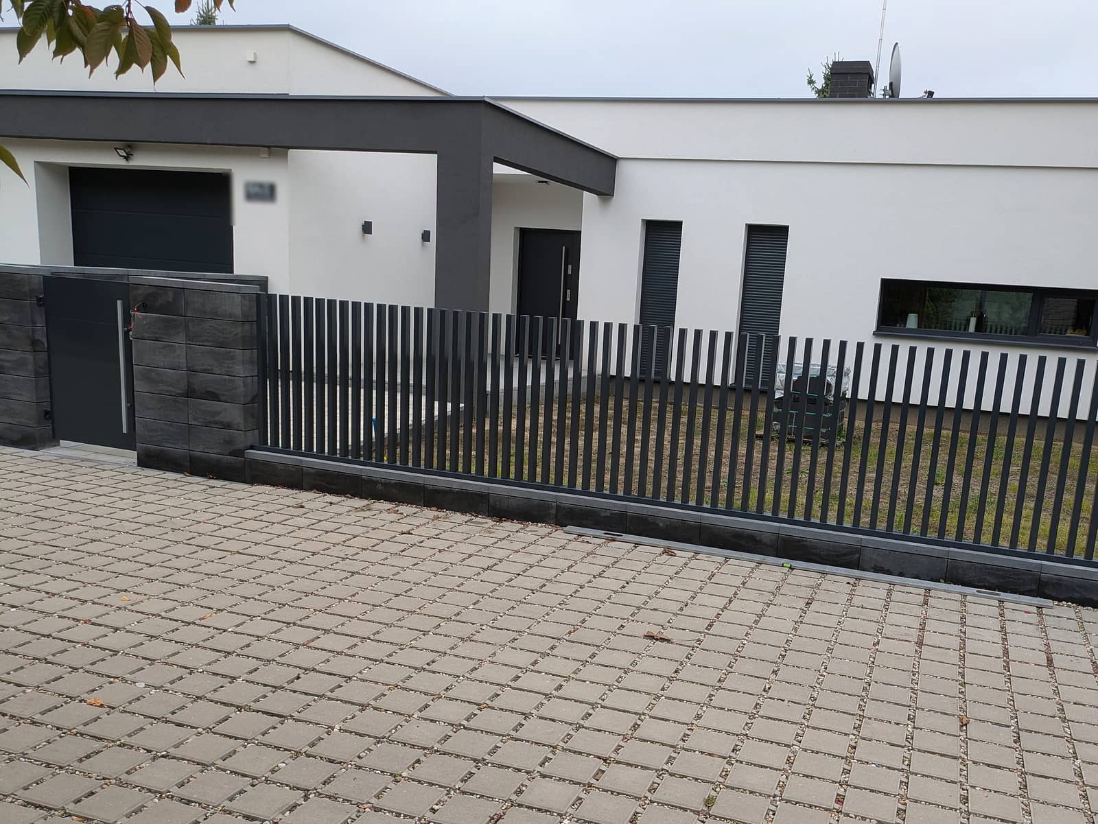Nowoczesne ogrodzenie z pionowych profili stalowych w kolorze antracytowym na podmurówce przed domem