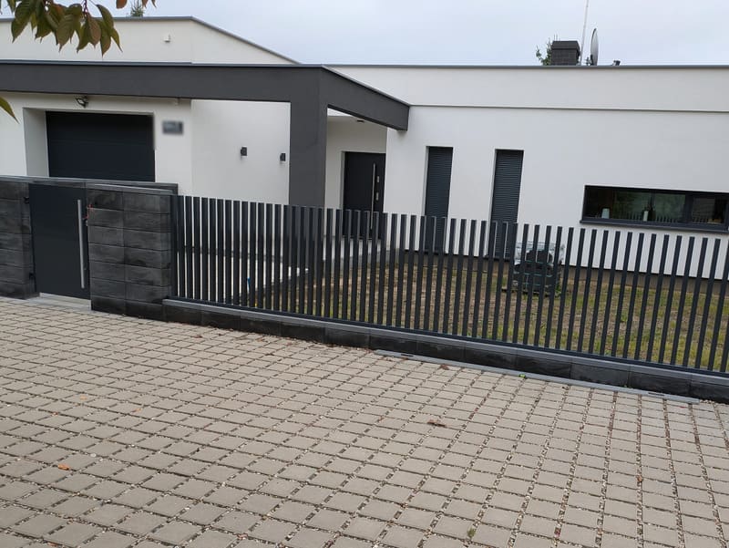 Nowoczesne ogrodzenie z pionowych profili stalowych w kolorze antracytowym na podmurówce przed domem