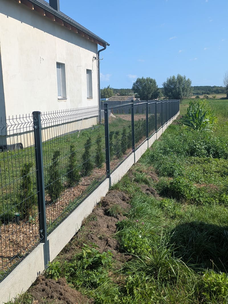 Ogrodzenie panelowe z podmurówką poprowadzone od narożnika domu wzdłuż granicy działki