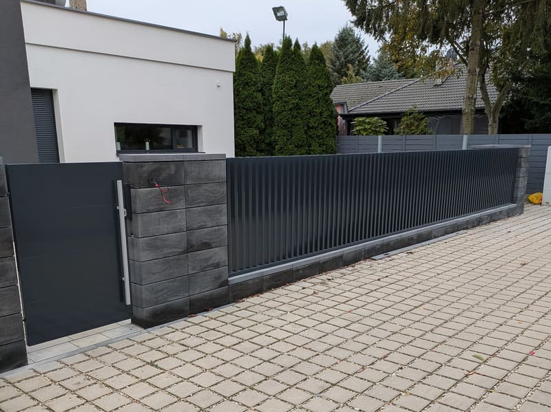 Ogrodzenie z pionowych profili i pełna furtka wzdłuż podjazdu z kostki ażurowej