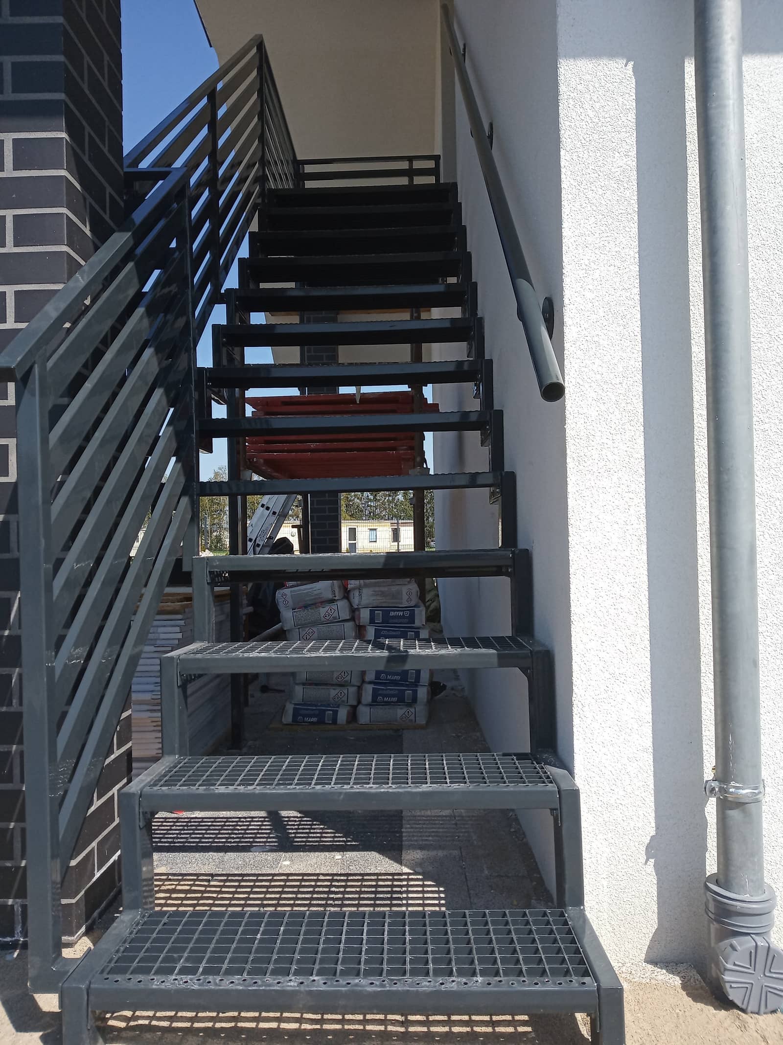 Stalowe schody zewnętrzne z podestem i balustradą przy elewacji budynku