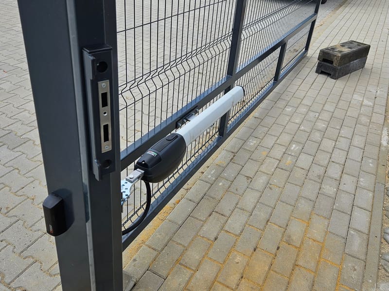 Siłownik i elektrozaczep na skrzydle bramy panelowej na terenie wyłożonym kostką brukową