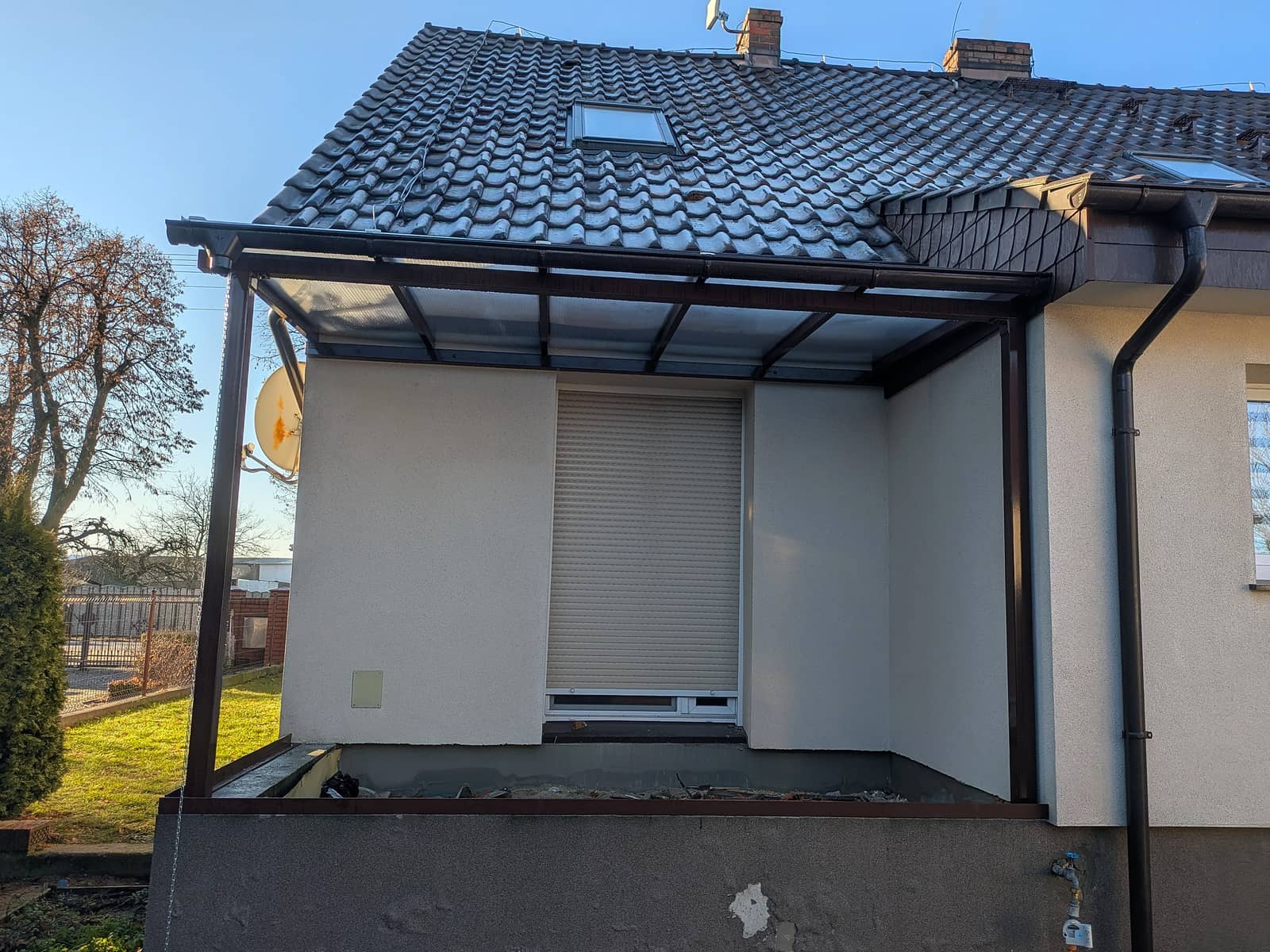 Zadaszenie wejścia do domu na brązowej konstrukcji stalowej z poszyciem z poliwęglanu